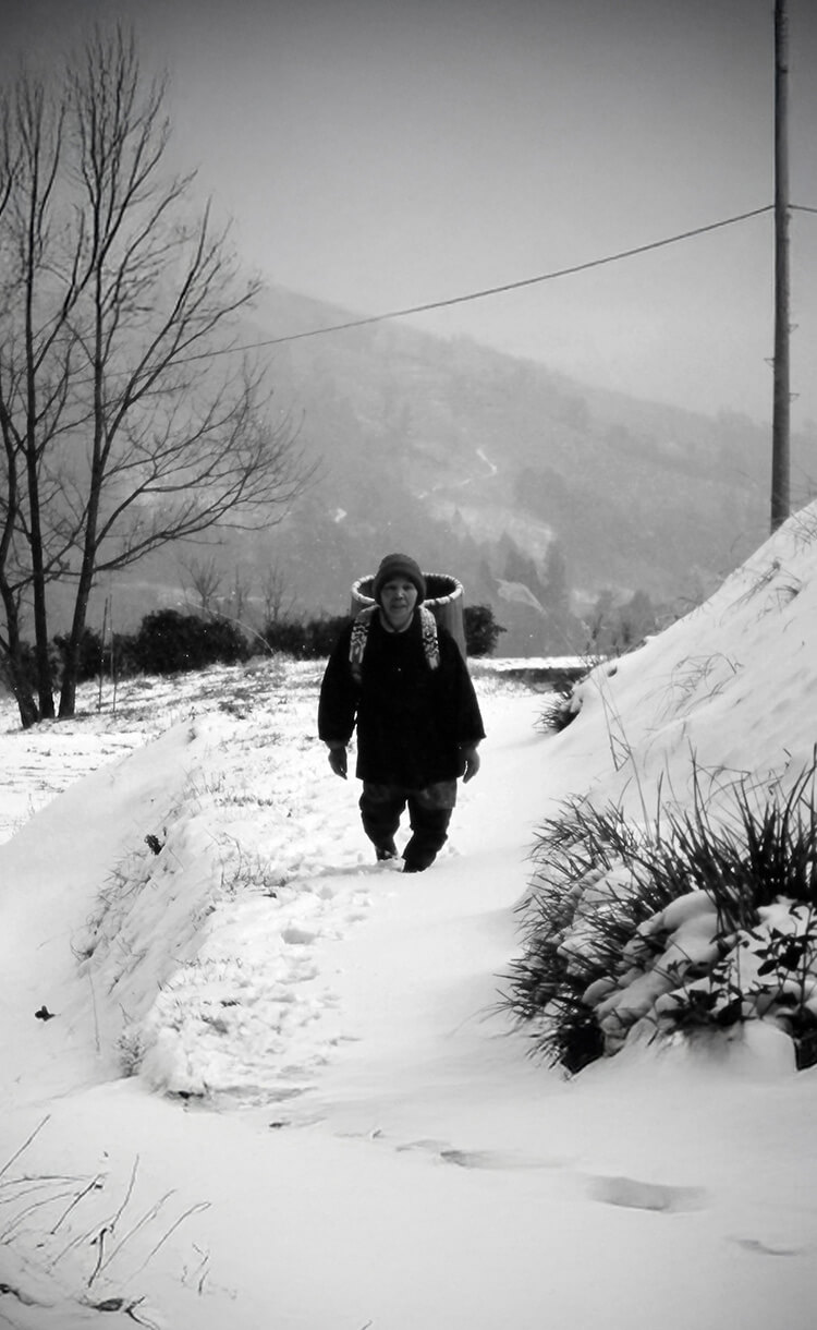 山奥の雪道を籠を背負って歩く老母